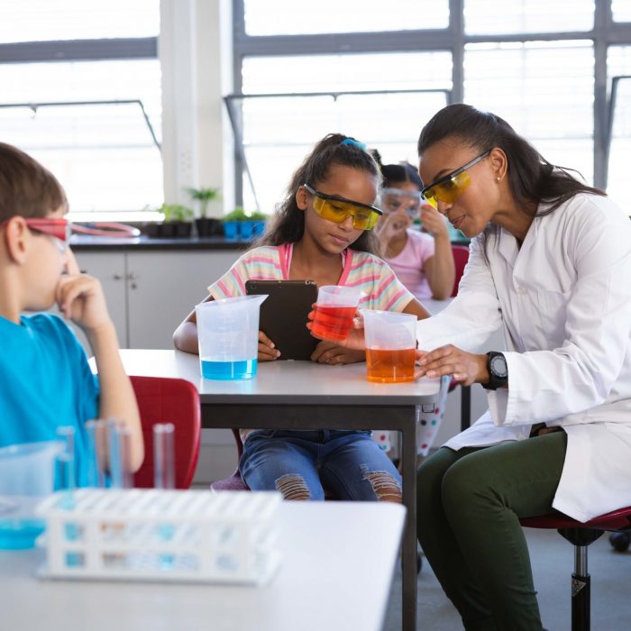 African american female teacher teaching chemistry to a girl during science class at laboratory. school and education concept